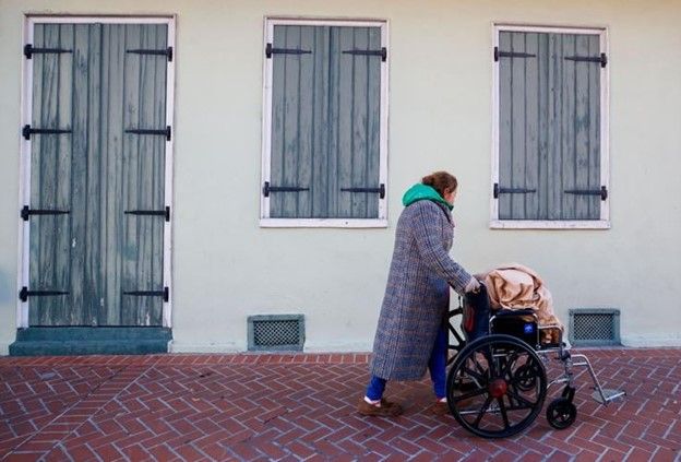A person in a heavy coat pushing a wheelchair down a brick-paved sidewalk.